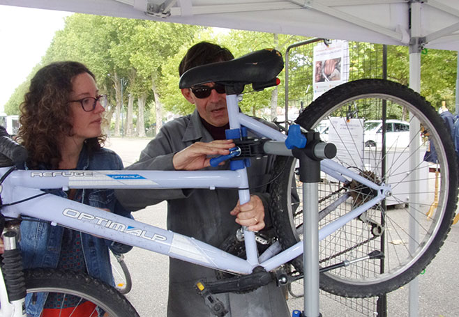 Photo de Gauthier sous le barnum, réparant le vélo d'une passante. 